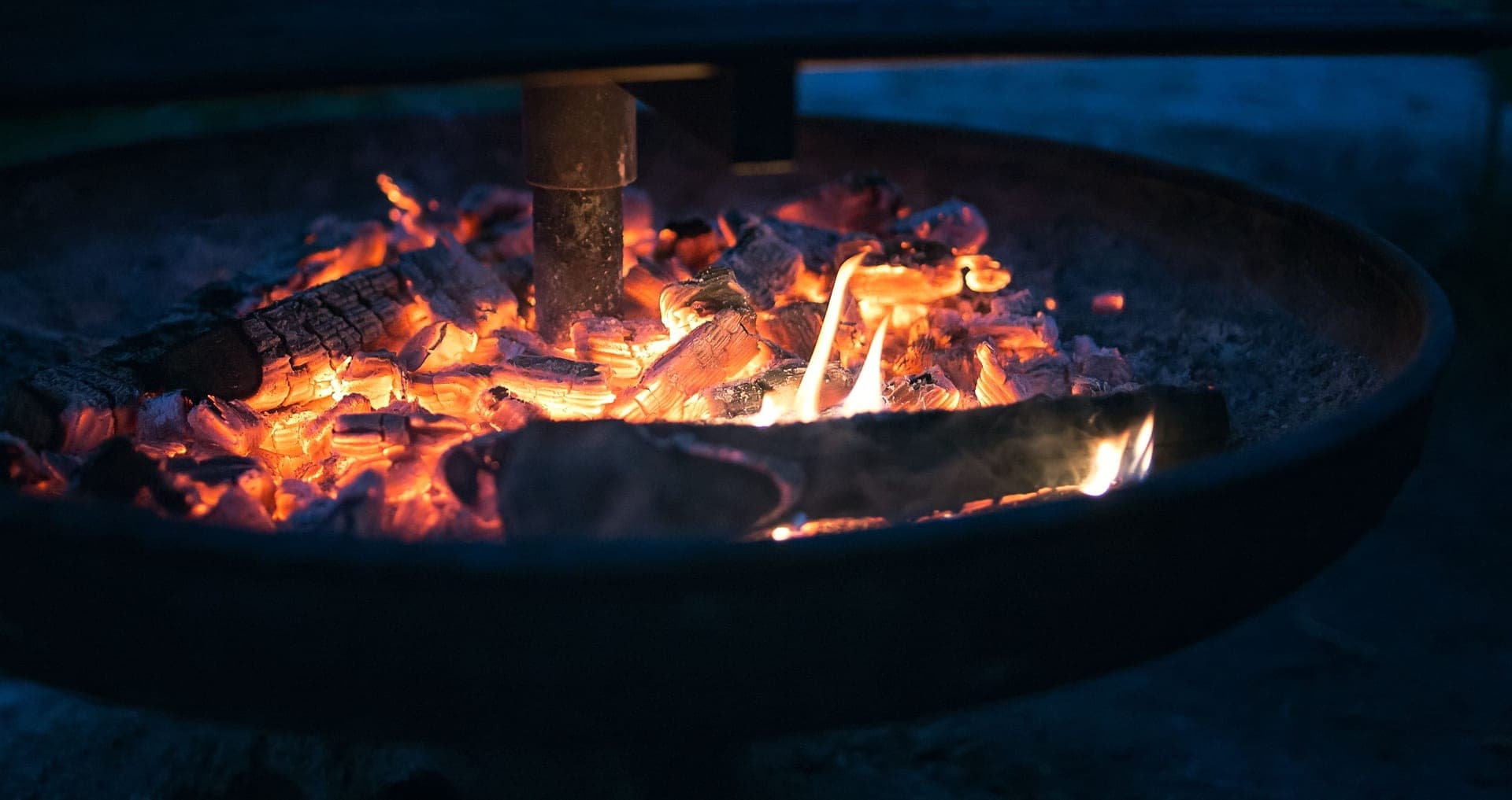 A wood fire burning down to embers in a round steel fire pit at dusk